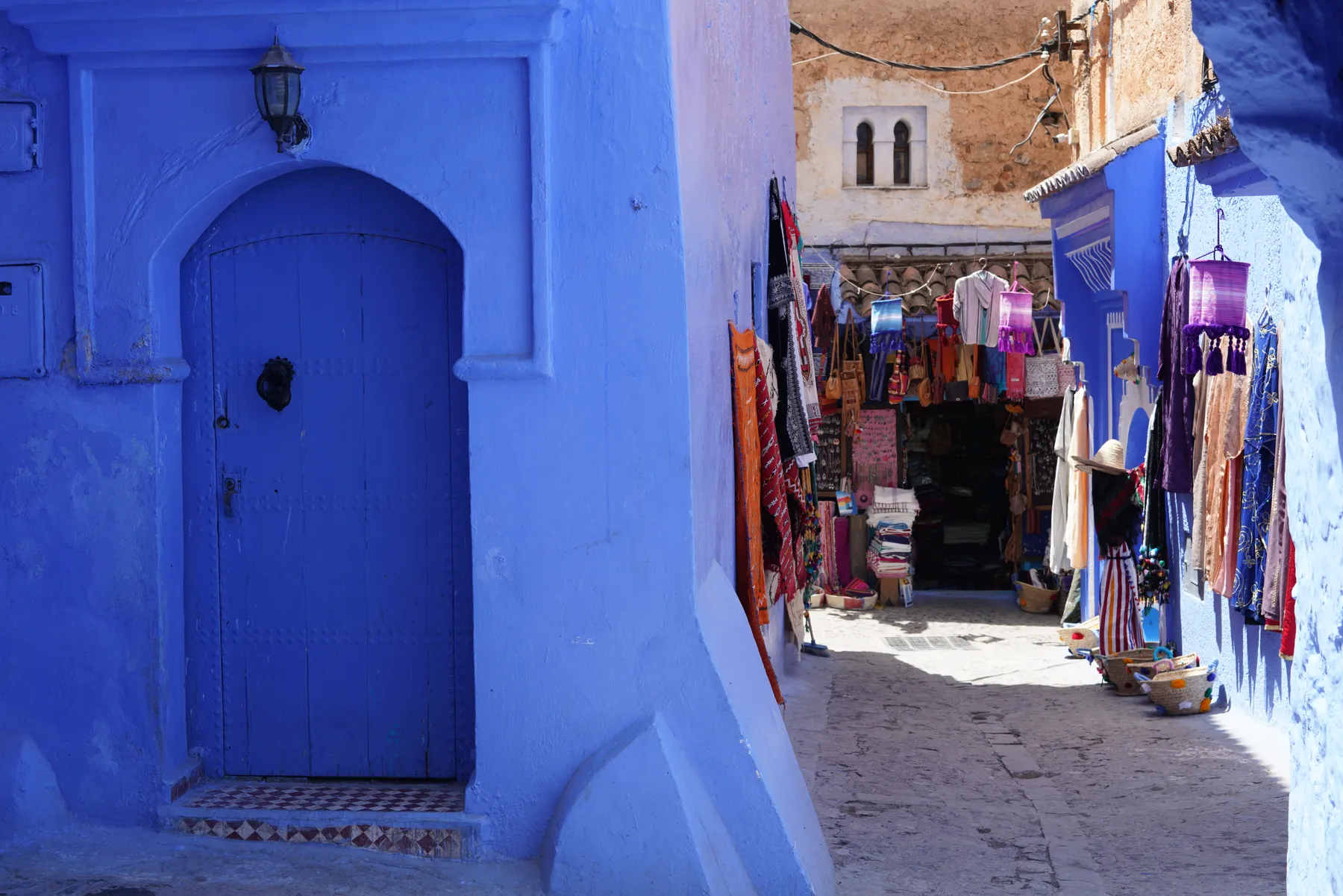 A blue door and hanging rugs in a lane of Chefchaouen