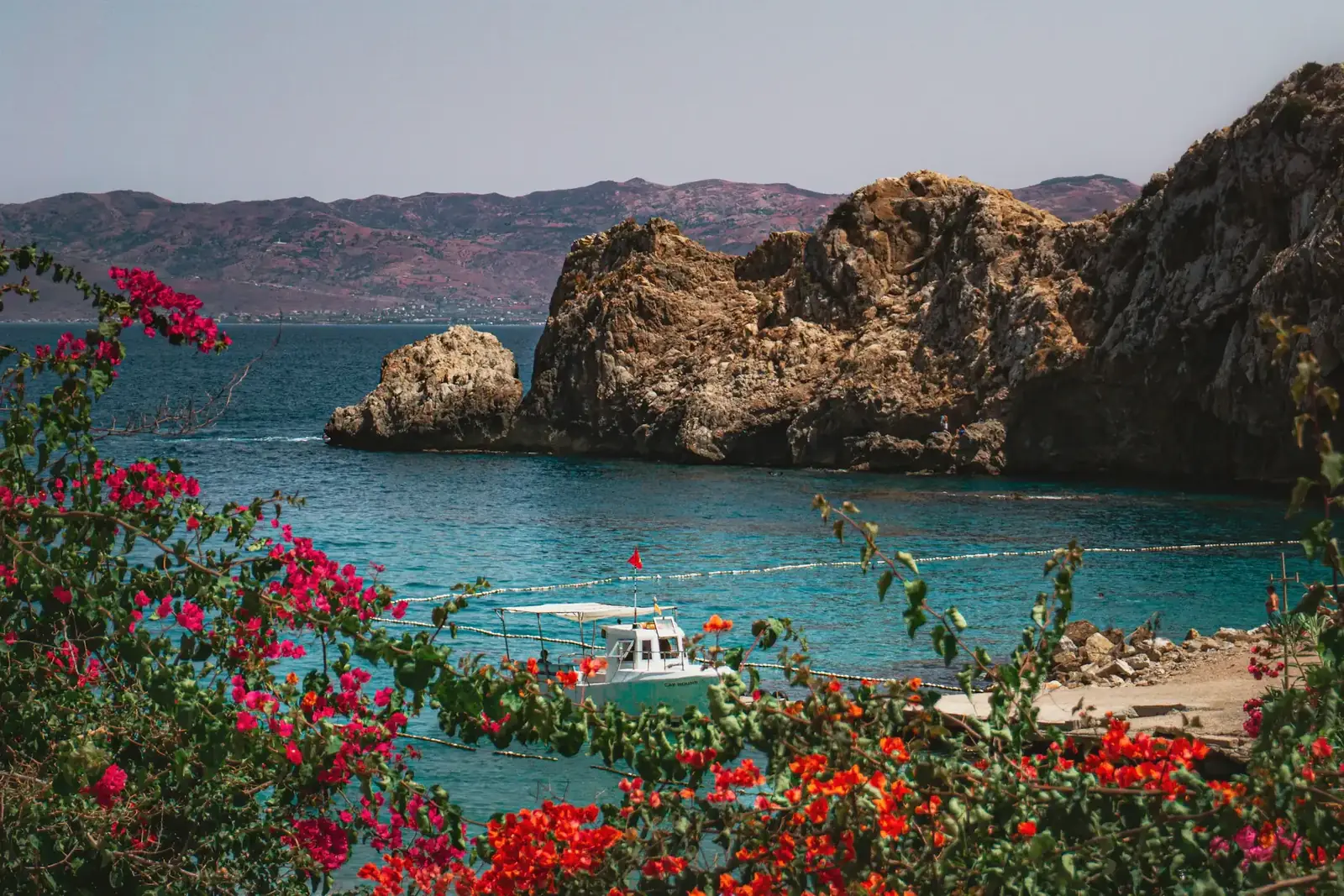 A turquoise cove under red cliffs on the Mediterranean coast near Al Hoceima, with flowers in front