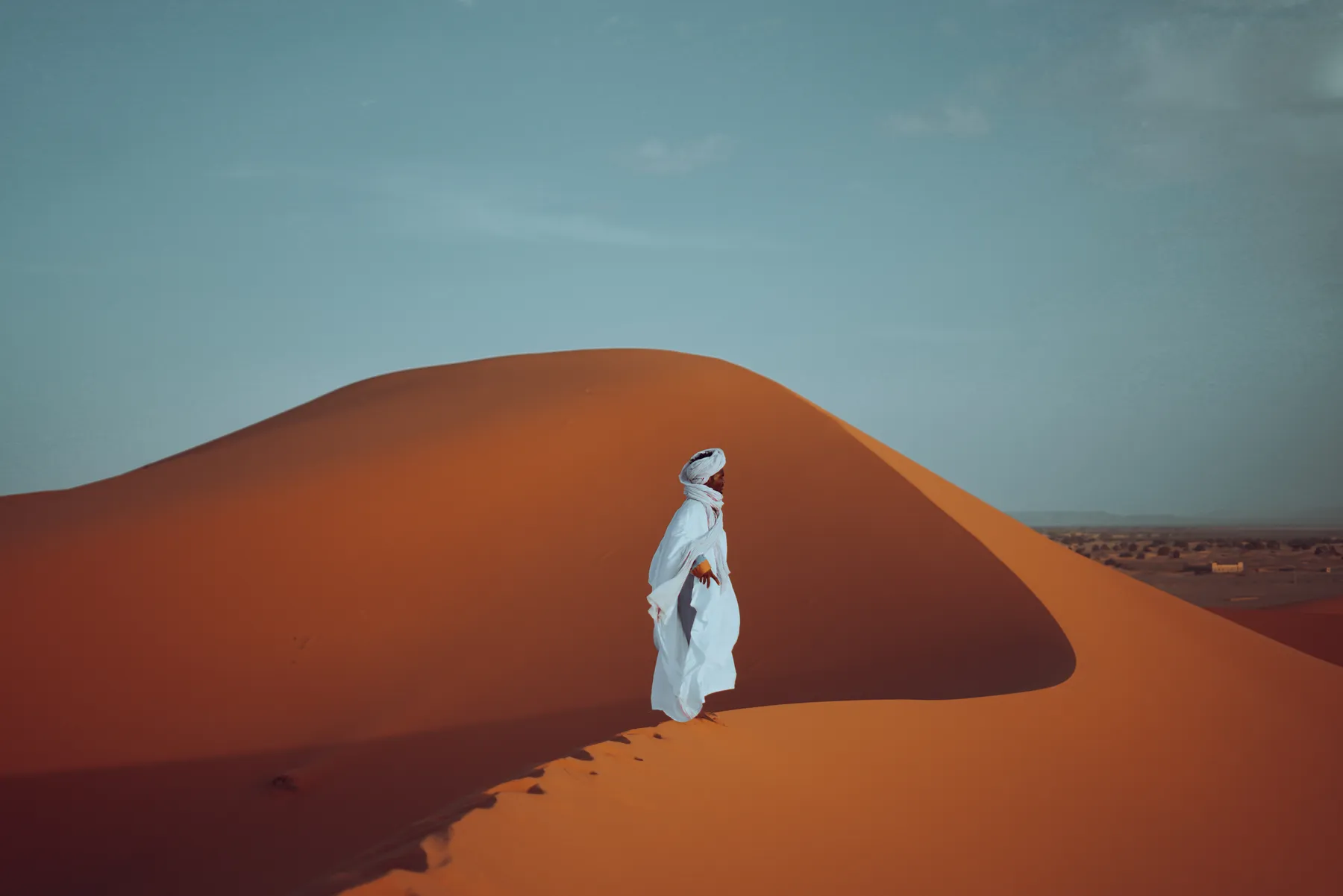 A man in a white robe standing on a red dune crest
